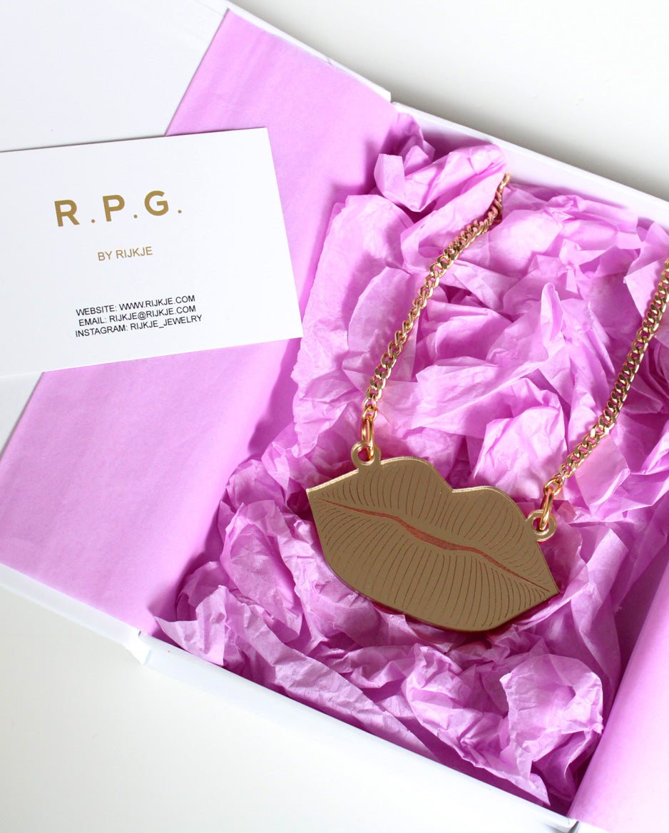 Goudkleurige ketting met lipvormige hanger in een doos met roze papier