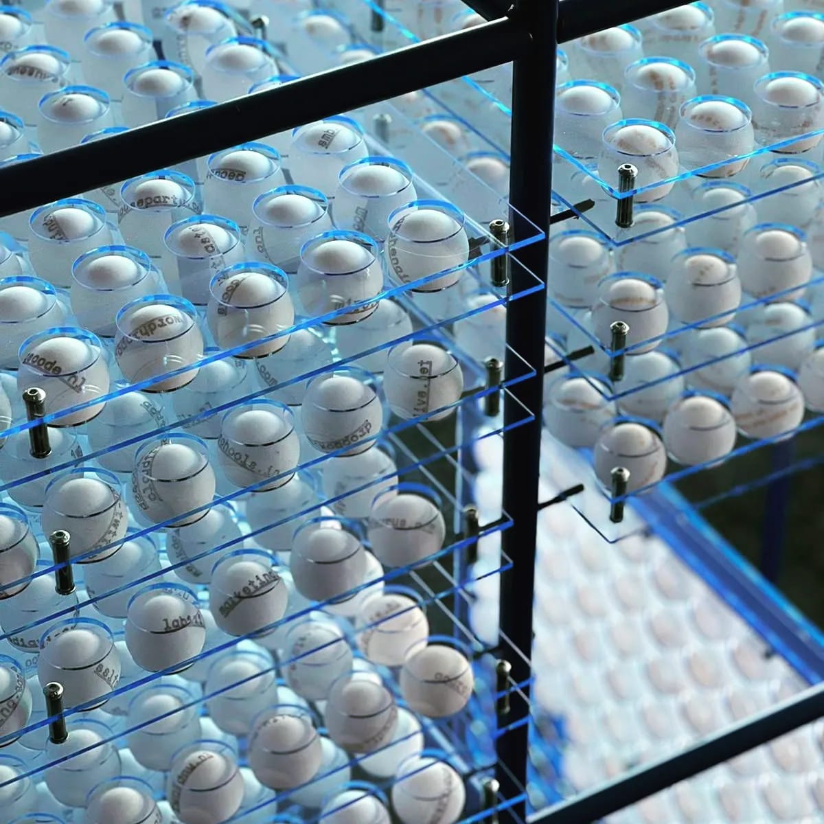 Tientallen witte pingpongballen in transparante houders binnen een zwart frame